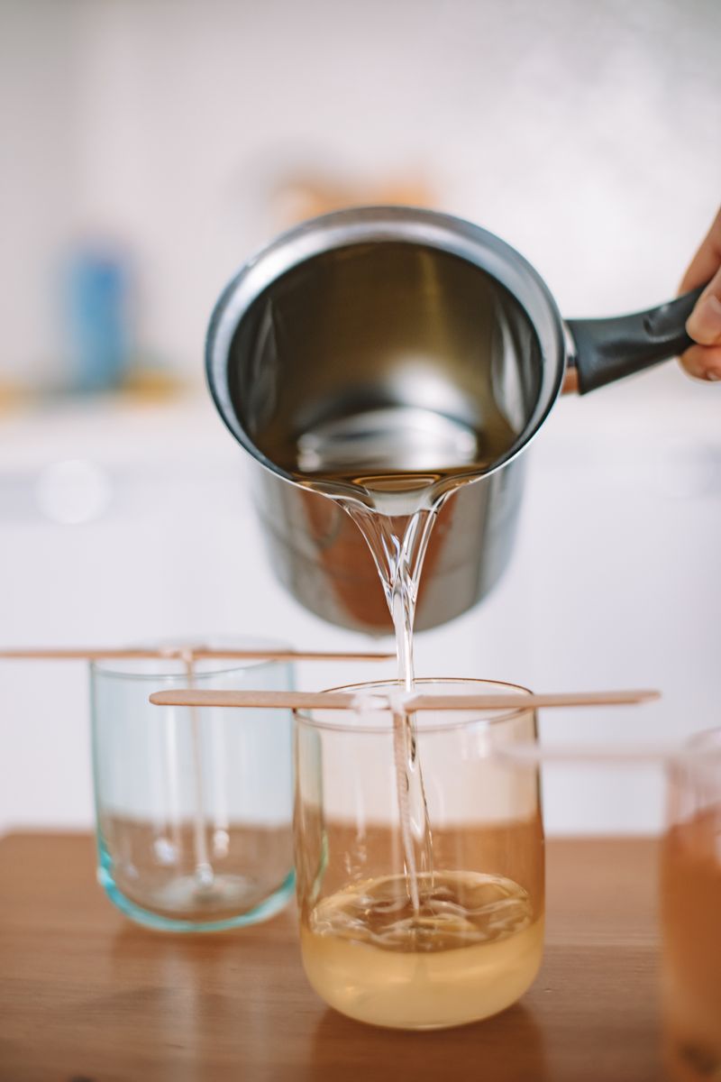 A candle maker hand-pouring soy wax into a jar